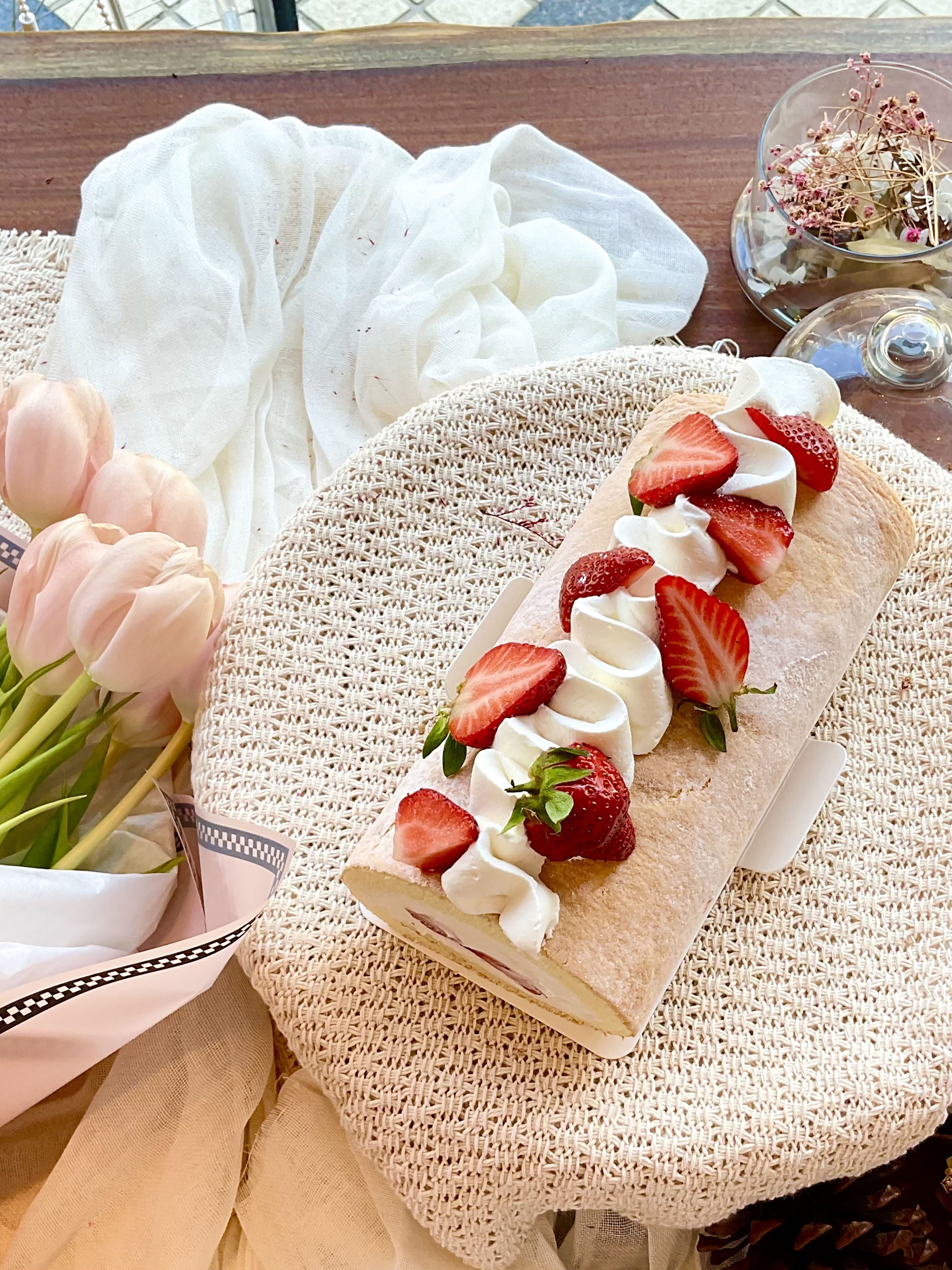 A homemade strawberry and cream roll cake beside pink tulips