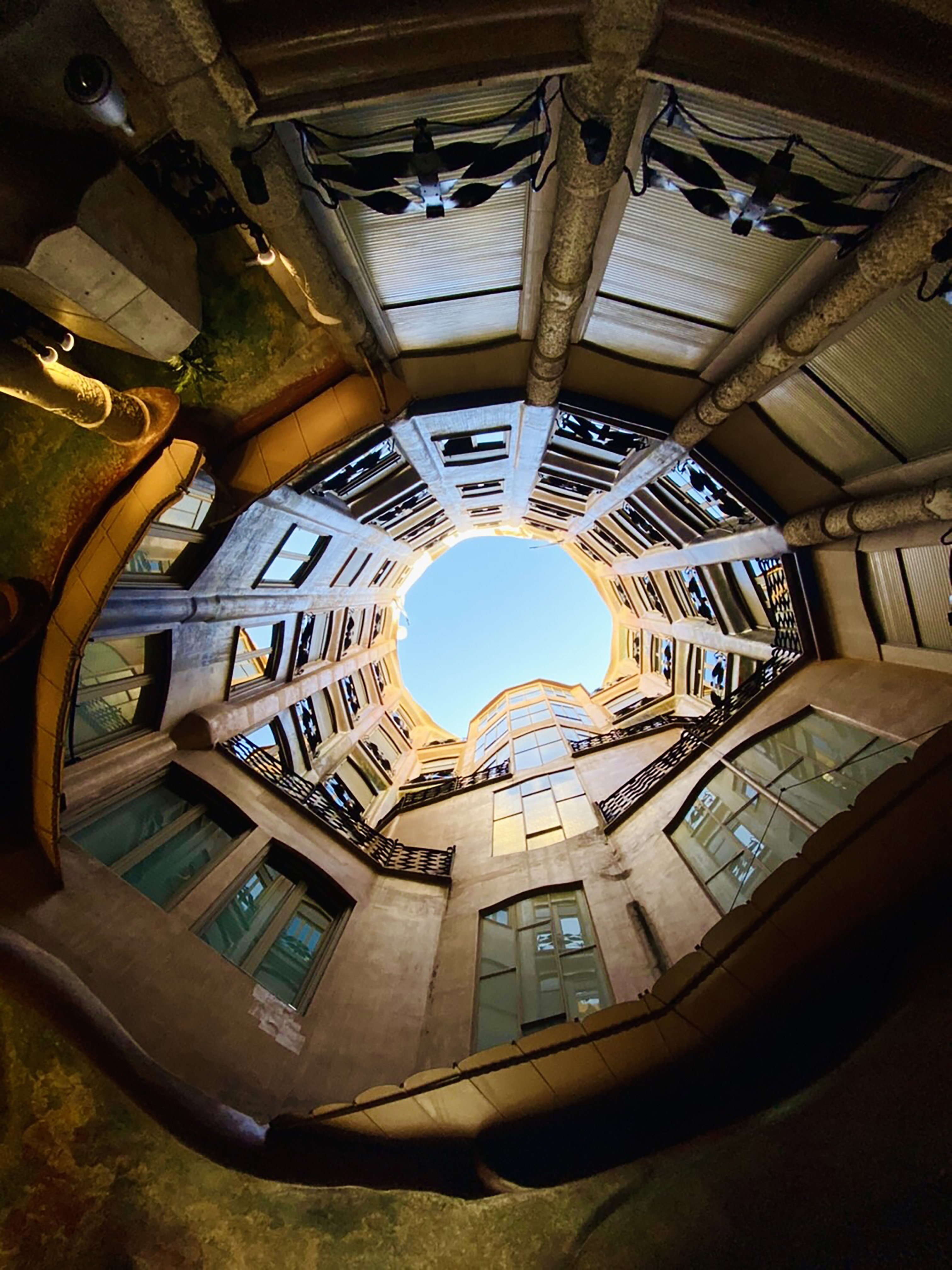 Looking up through a curved stone courtyard toward a patch of blue sky